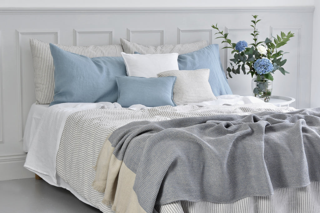 A Stripe Linen Duvet Cover on a Bed with Blue Linen Cushions and a bedside table of flowers
