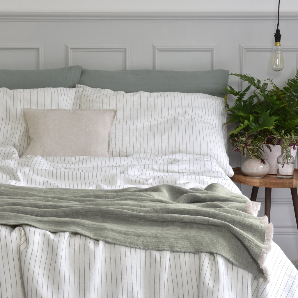 A Sage Green Linen Throw on a Bed with A Natural Linen Striped Duvet Cover and Green Linen Pillowcases