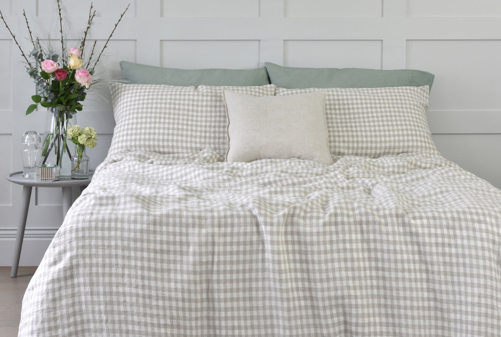 A Beige Gingham Bed Set on a Bed with Sage Green Linen Pillowcases and Pink Roses in a Vase on a Side Table