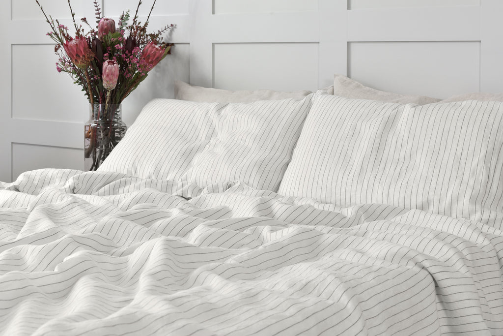 A Stripe Linen Duvet Cover on a Bed with Pillowcases and a Bedside Table with Pink Flowers on