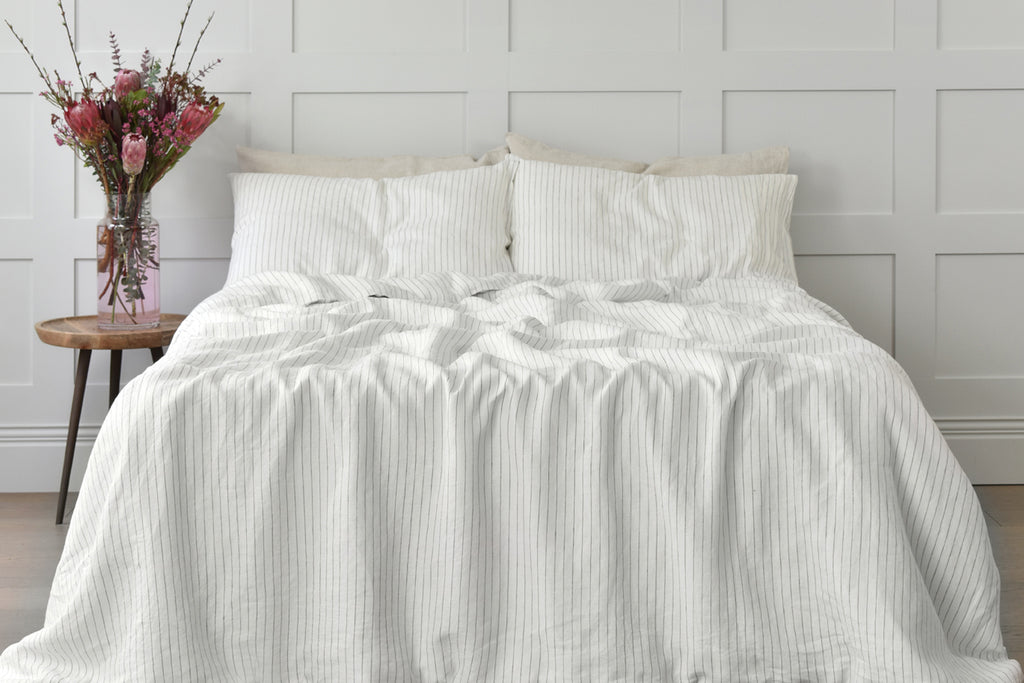 A Pinstripe Linen Duvet Cover on a Bed in a Bedroom with Paneled Walls and a Bouquet of Pink Flowers