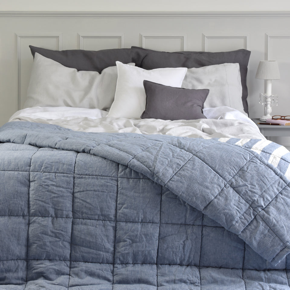 A Blue Chambray Stripe Linen Quilted Bedspread on a Bed with White Linen Sheets and Grey Linen Pillowcases