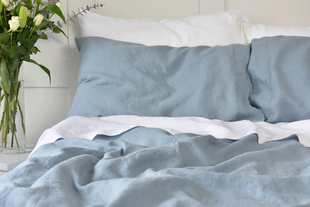 A Blue Linen Pillowcase on a Bed with a White Linen Sheet.
