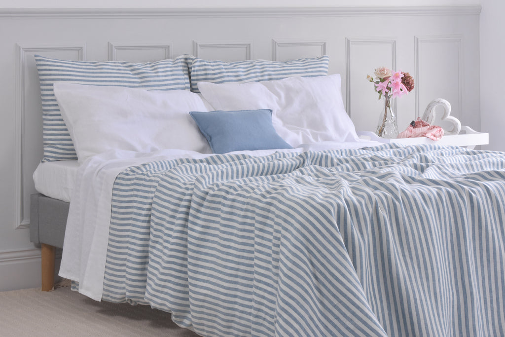 A Blue Stripe Ticking Linen Duvet Bed Set on a Bed with White Linen Pillows and a Vase of Pink Flowers on a bedside cabinet