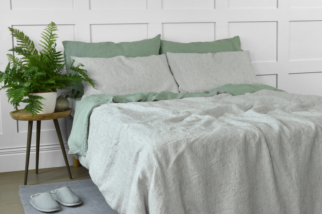 A Stripe Linen Duvet on a Bed with Green Linen Pillowcases and a Side Table with a Green Fern Plant