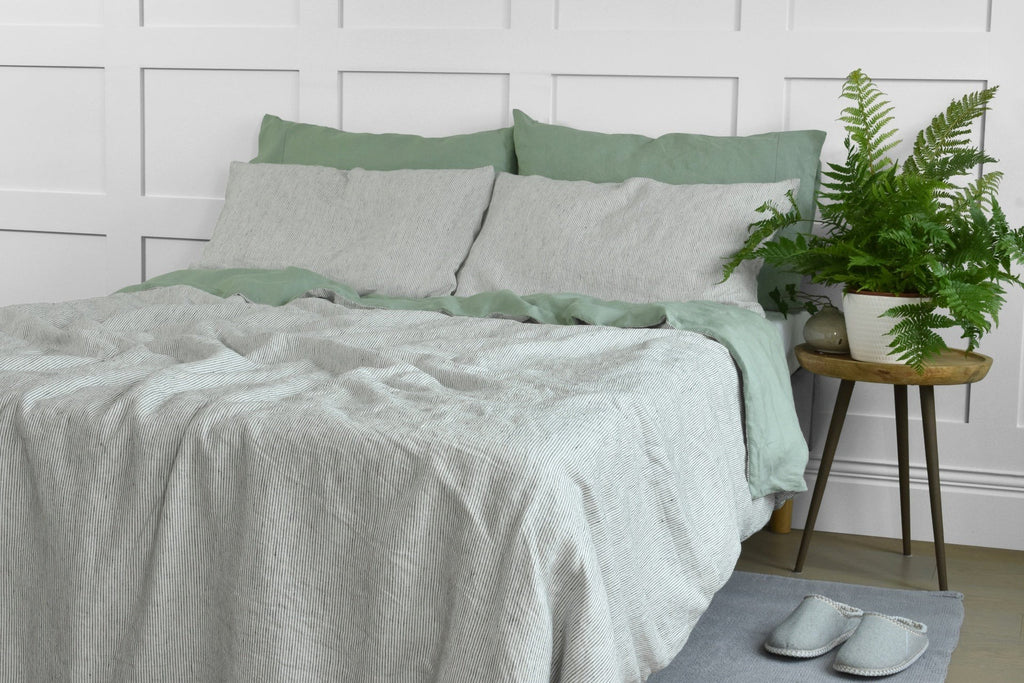 A Double Sided Pinstripe Linen Bed Set on a Bed with Green Linen Pillowcases