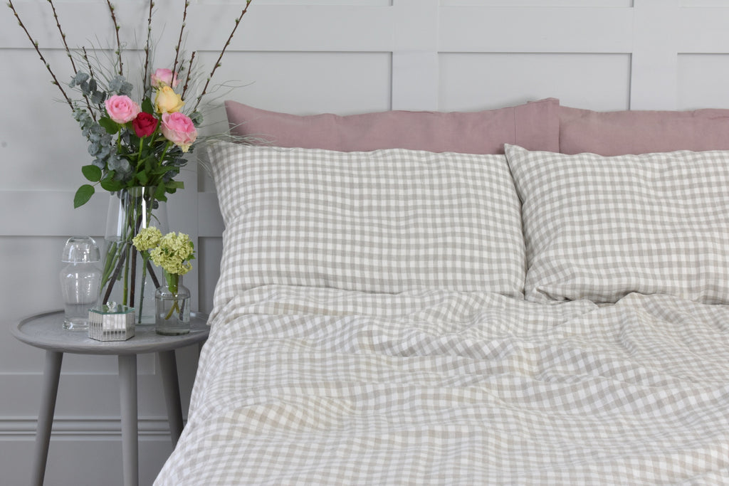 A Bed with Natural Gingham Linen Pillowcases and Pink Linen Pillowcases next to a Vase of Pink Roses