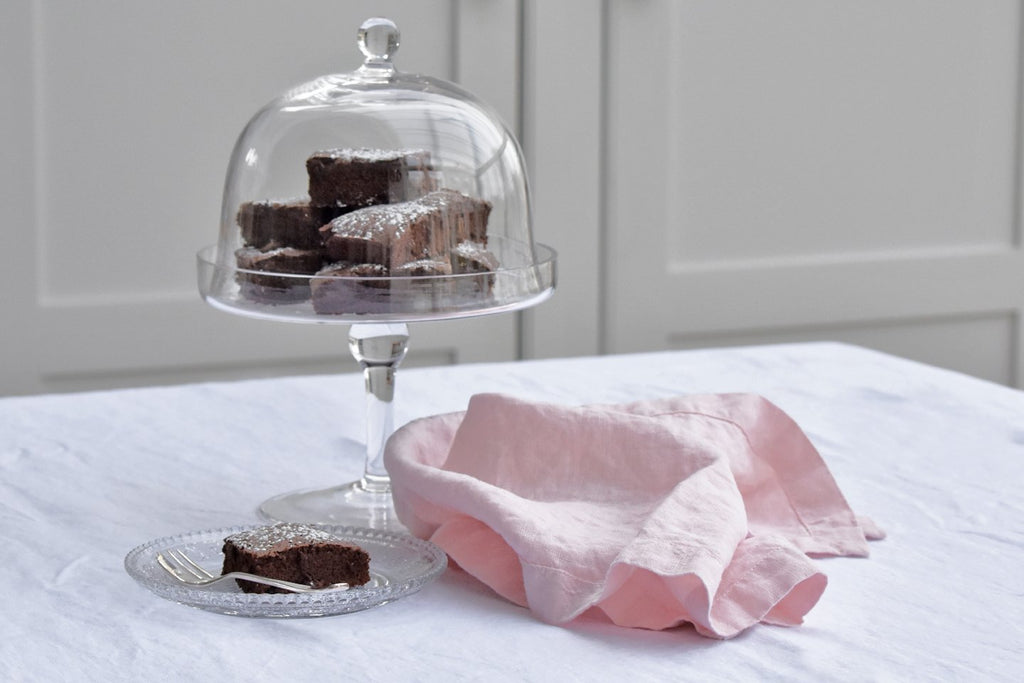 A Pink Linen Napkin on a Table with a Cake stand full of Chocolate Brownies