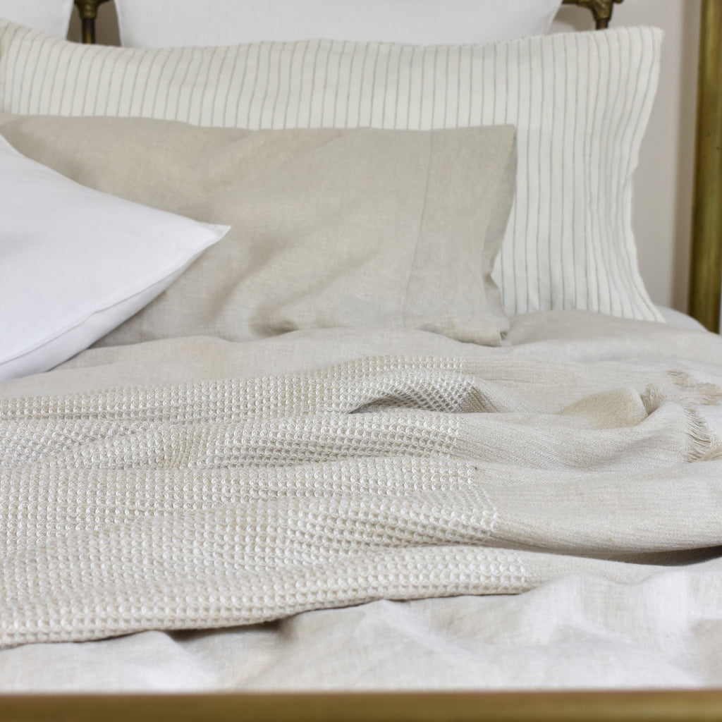 An Oatmeal Linen Blanket on a Bed with White Linen Sheets and bedside table with flowers