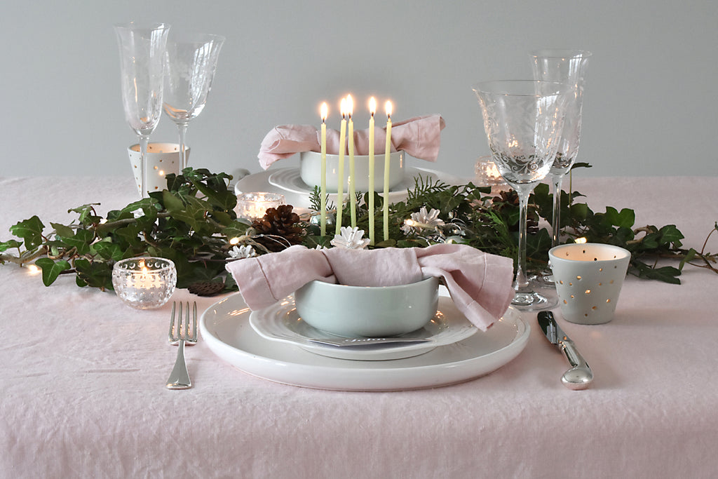 Elegant table setting with candles, greenery, and pastel colors on a pink tablecloth.