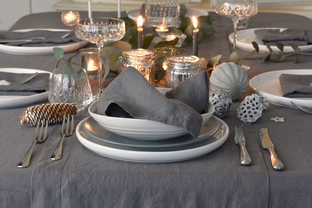 Elegant table setting with gray napkins, plates, and silverware on a gray tablecloth.