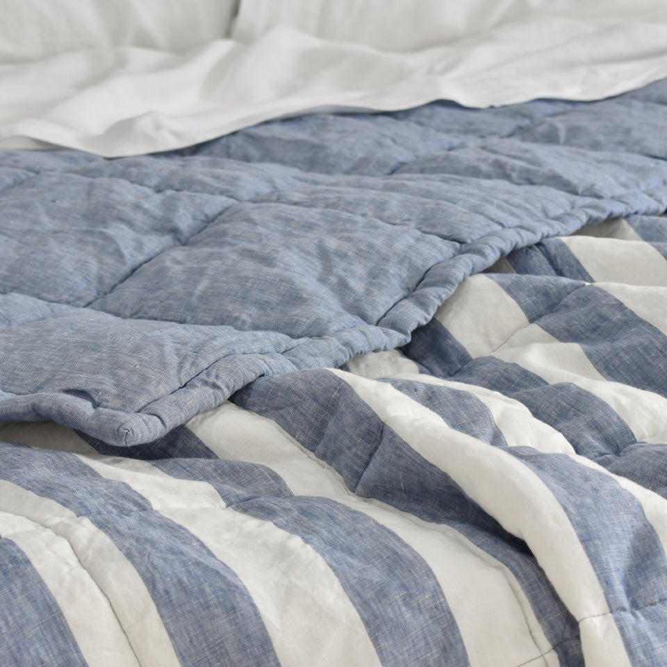 A Chambray Stripe Linen Quilt with the corner folded back on a Bed with White Linen Sheets