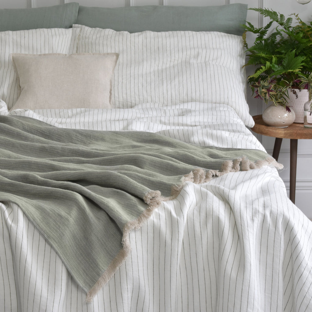 A Woven Linen Blanket on a Bed with a Stripey Linen Duvet Set