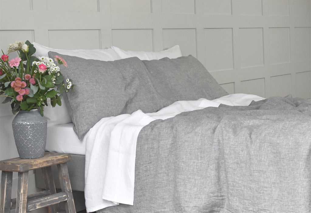 A Soft Grey Linen Duvet Cover and Pillowcases on a Bed with a Bedside Table with Pink Flowers