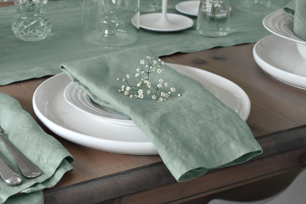 A Sage Green Linen Napkin on a White Plate with White Flowers on top