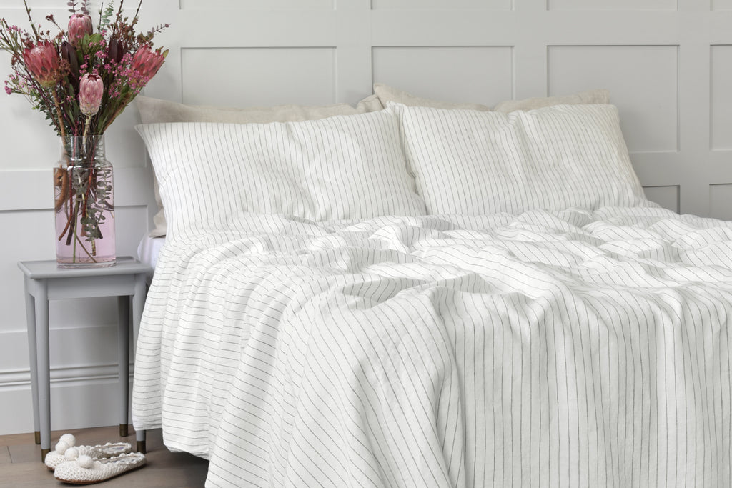 A Cream Stripe Linen Duvet Cover on a Bed in a Bedroom with Paneled Walls and a Bouquet of Pink Flowers