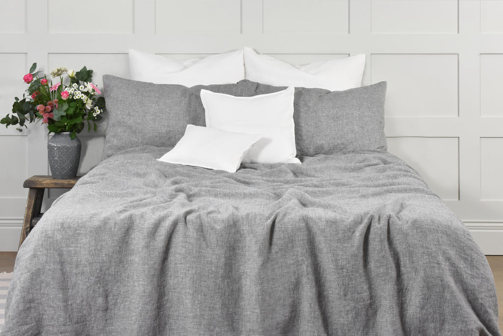 A Granite Grey Duvet Cover set on a Bed with White Linen Cushions and Pink Roses on a Bedside Table