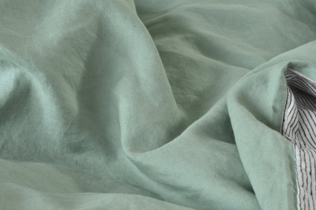 A close up Photo of a Piece of Sage Green Linen Duvet Cover with a Pinstripe Linen Back