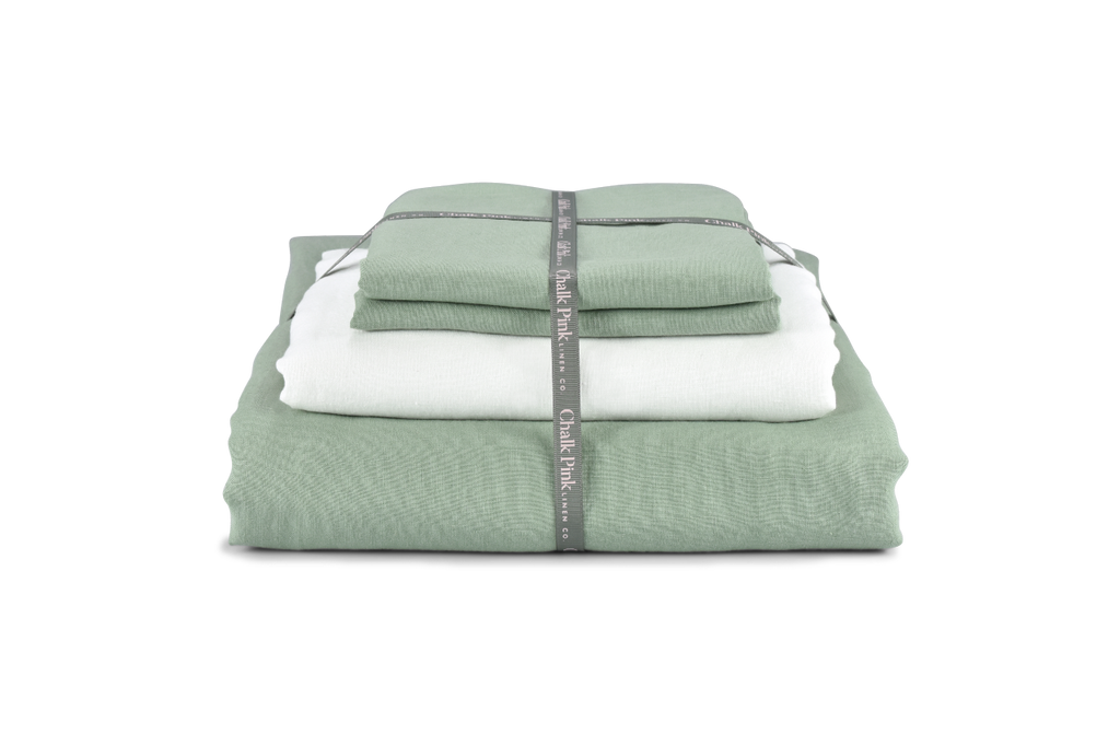 A Folded Green Linen Bedding Set with a White Linen Sheet with Ribbon tied around for a Gift