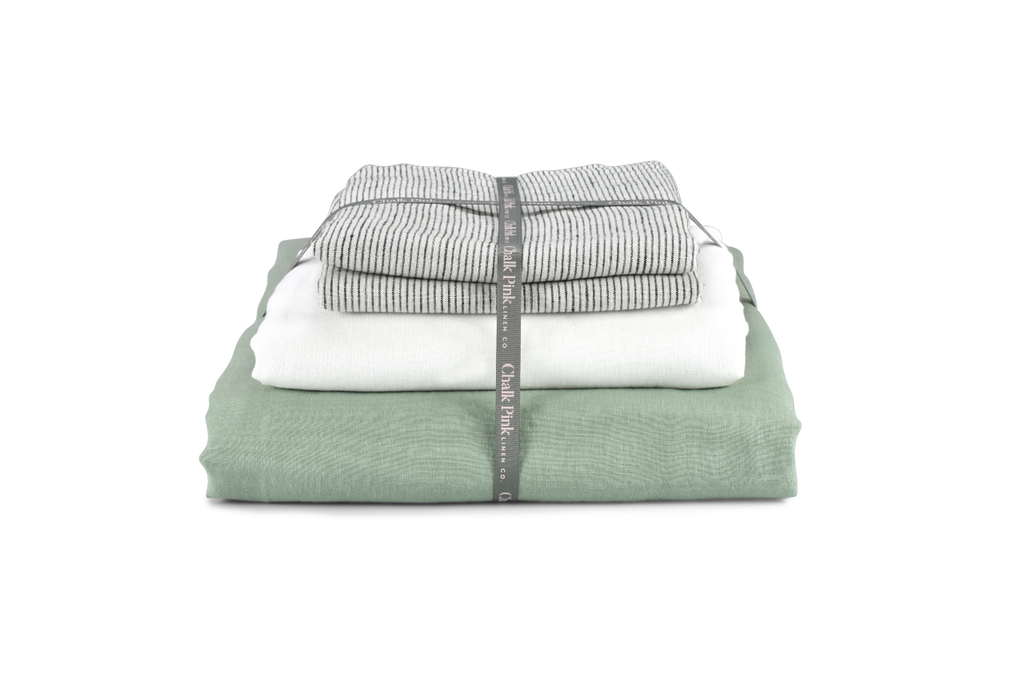A folded Green Linen Double Sided Duvet Cover  with a Folded White Linen Sheet and Pinstripe Linen Pillowcases with Ribbon around them