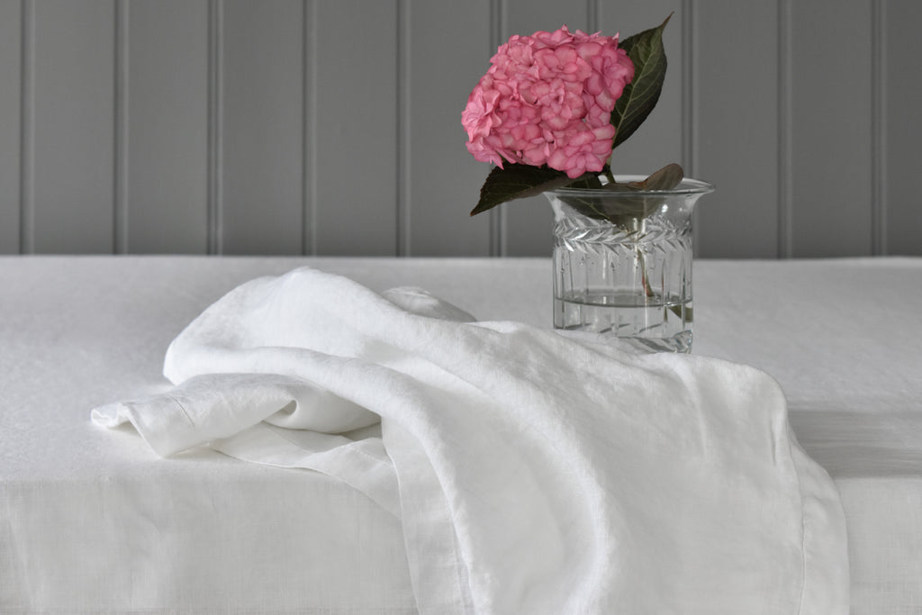 A White Linen Napkin on a Table with a Pink Flower